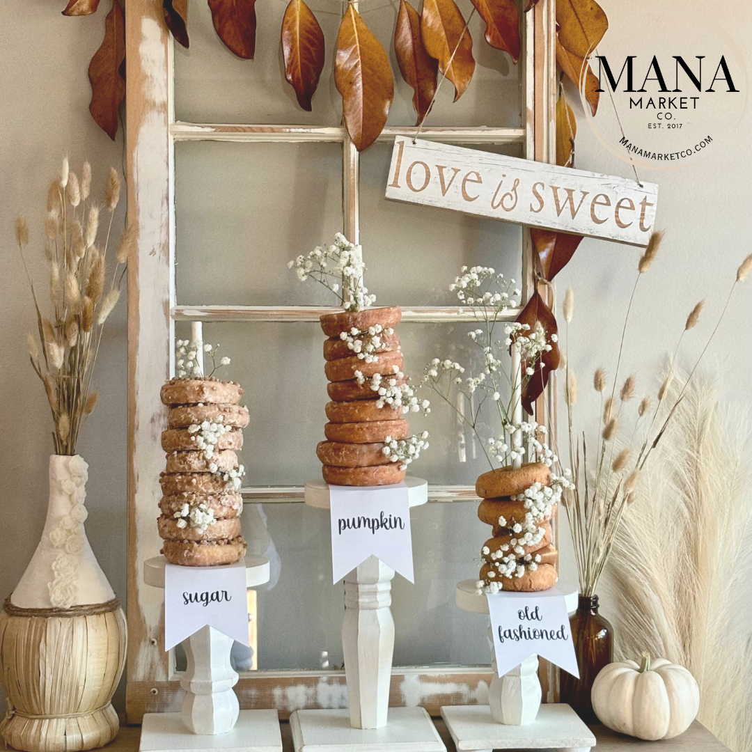 A set of donut bar tags displayed on a white stand, with 'love is sweet' sign in the background, arranged on a table with decorative leaves and a pumpkin-shaped center piece.