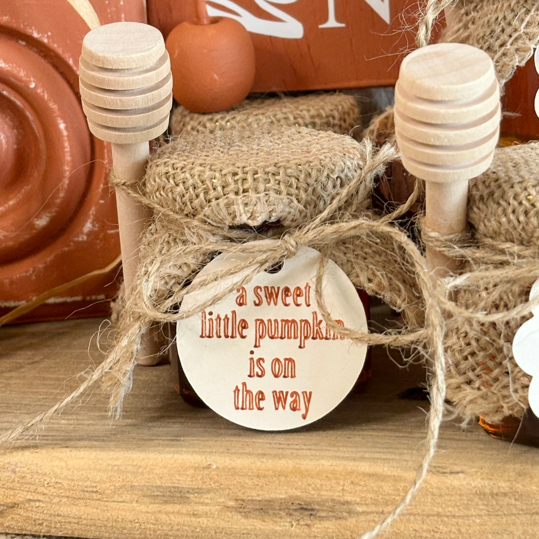 Decorative item with 'a sweet little pumpkin is on the way' tag, surrounded by burlap and pumpkins.