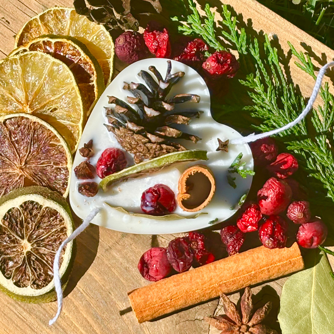 Decorative heart-shaped ornament with pine cones, berries, and cinnamon on a wooden surface.