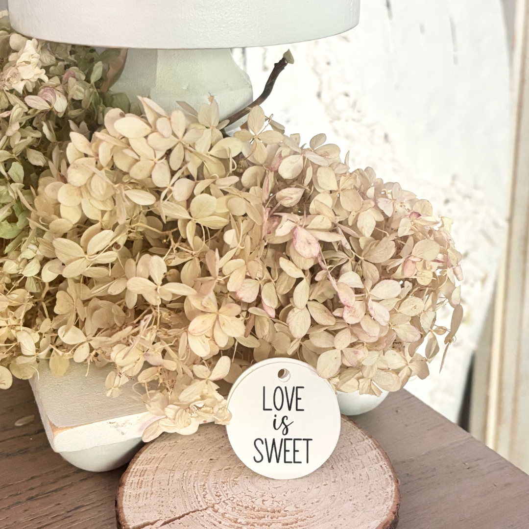 Decorative arrangement of dried flowers with a 'Love is Sweet' tag on a wooden surface.