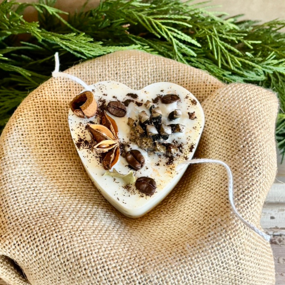 Heart-shaped candle with coffee beans and star anise on a burlap surface with greenery in the background