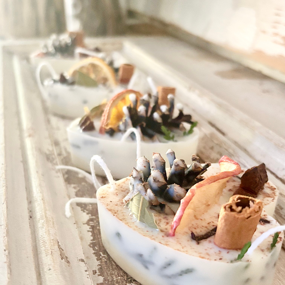 Decorative candles with pine cones and cinnamon sticks on a marble surface.