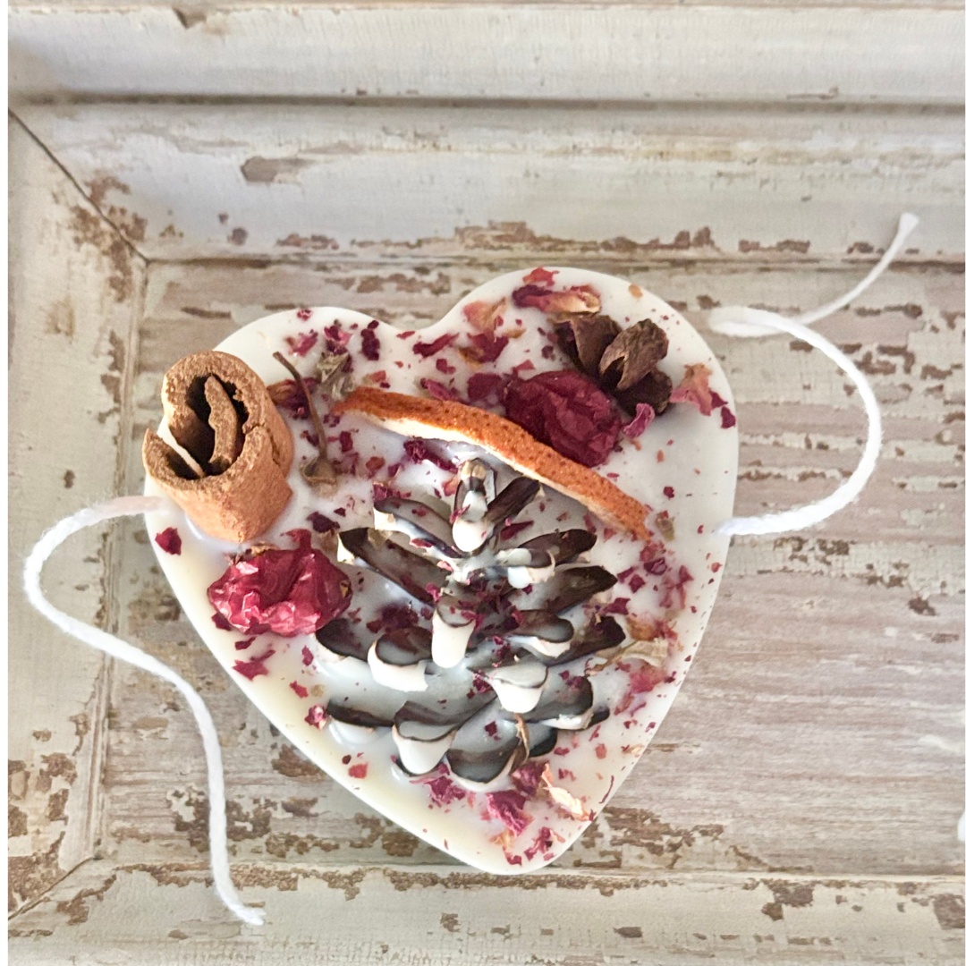 Heart-shaped decorative item with pinecones, flowers, and twigs on a rustic wooden surface